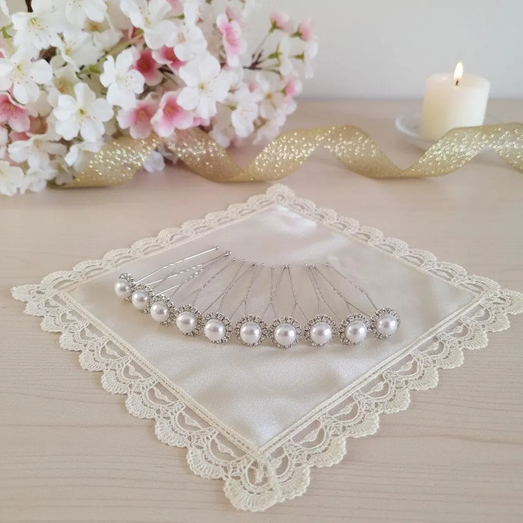 Épingles à chignon avec perles blanches nacrées et strass, disposées en éventail sur un coussin en satin bordé de dentelle.